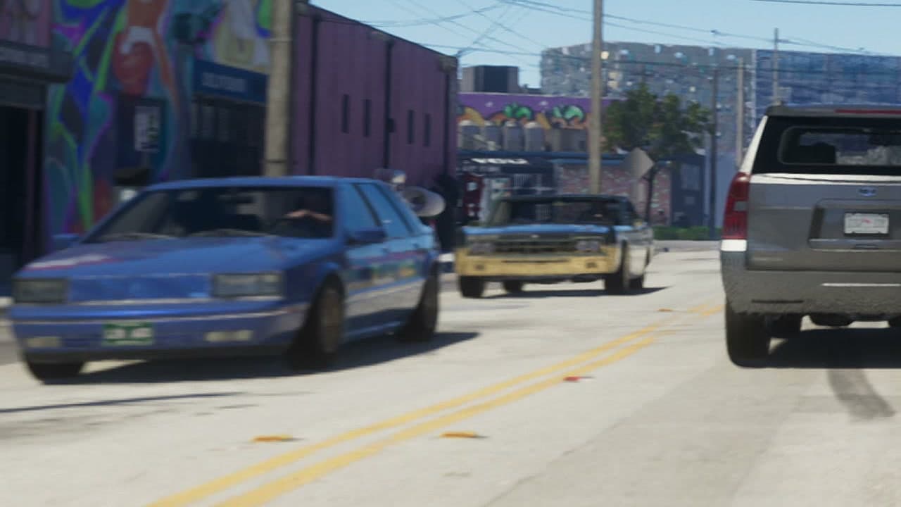 Berlina azul circulando por una calle con murales de Stockyard, en el tráiler 1 de GTA VI