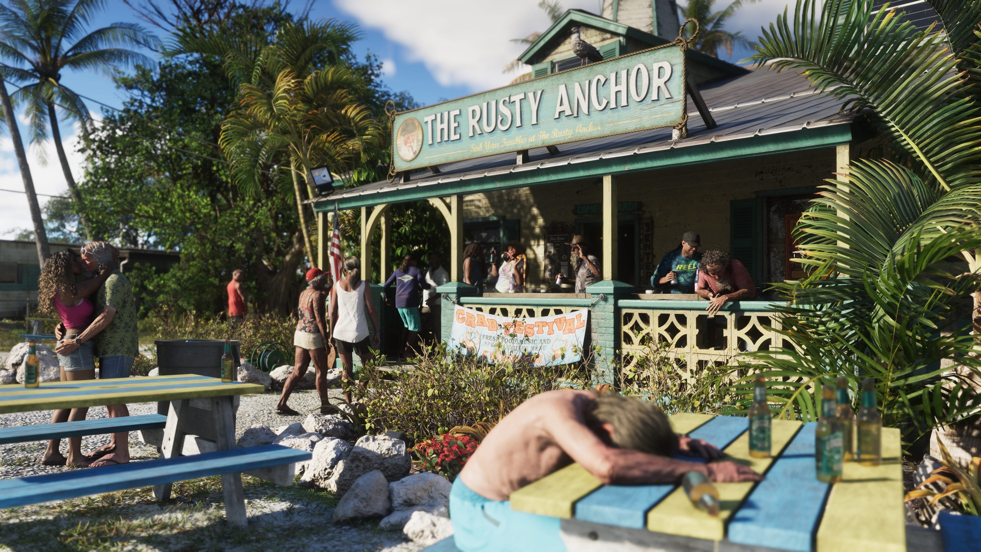 Wooden beach bar called The Rusty Anchor with customers on the porch and a man lying on a bench by the palm trees.