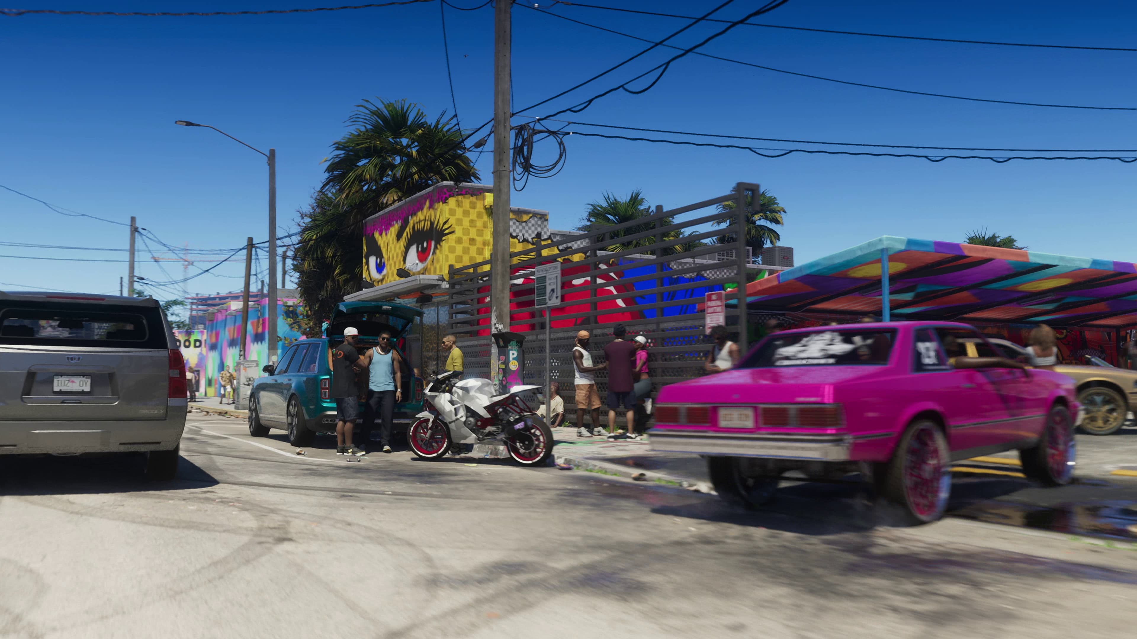 Custom cars and people beside colorful murals on a Stockyard street