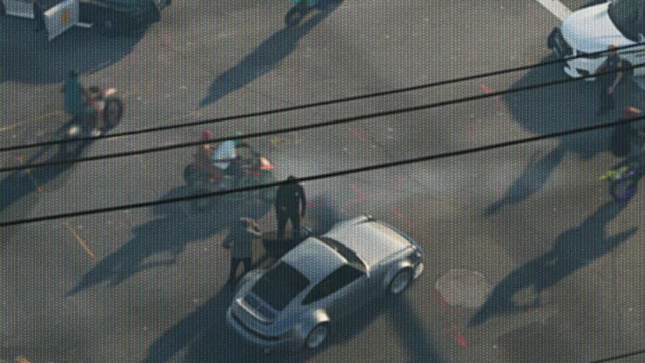 Silver sports car seen from a helicopter at a Vice City intersection, surrounded by police and dirt bikes, in GTA VI Trailer 1
